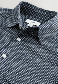 Camisa de cuadros en color navy con patrón de cuadrícula blanca, material de algodón, cuello clásico y botones blancos. La etiqueta indica talla M.