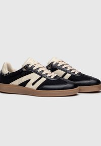 Sneaker neri e crema con una tomaia in pelle liscia, dettagli in morbido tessuto, suola in gomma e strisce a contrasto sui lati.
