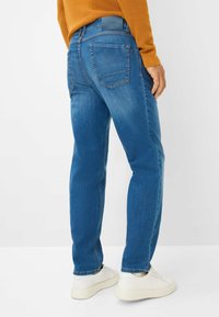 Jeans in denim blu con vestibilità a gamba dritta. Presentano due tasche posteriori e una cintura con marchio. Abbinati a sneaker bianche.