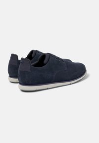 Marineblauwe suède veterschoenen met een gladde textuur, ronde neus en een witte rubberen zool met een subtiele paarse accent op de middenzool.
