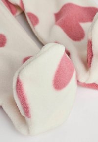 Tissu en polaire blanche avec de grands motifs en forme de cœur rose. La texture est douce et moelleuse, présentant des bords arrondis et des détails enroulés.