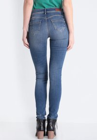 Jeans de denim ajustados en azul medio con una textura suave, cintura de altura media y un sutil desgaste en los muslos, combinados con botas negras de tobillo.
