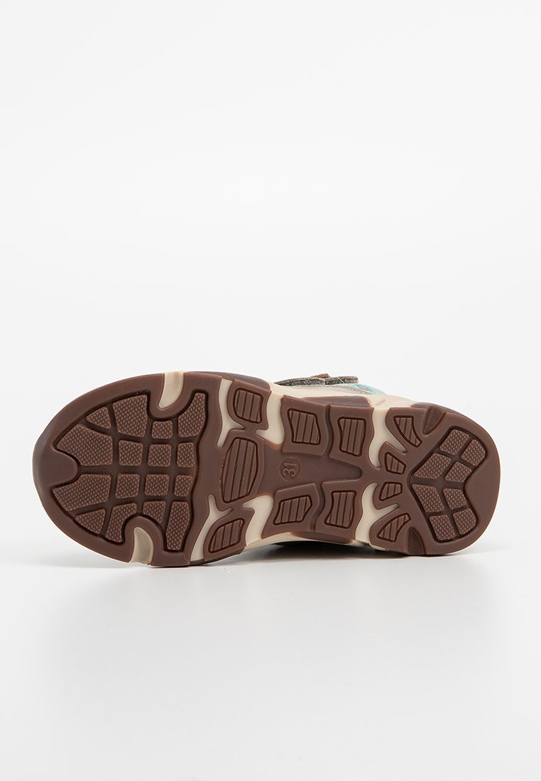 Brun gummiyttersida med texturerat greppmönster. Har kontrasterande beige detaljer och en robust design för dragkraft och hållbarhet.