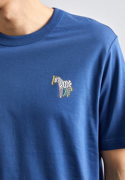 Mėlynas apvalios kaklo marškinėliai pagaminti iš minkštos medžiagos, su mažo, spalvoto zebro piešiniu kairėje krūtinės pusėje.