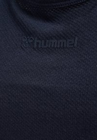 Marinblå sportstopp i texturerad tyg. Har en subtil logotyp i svart vid halsringningen och visar en närbild av materialet.