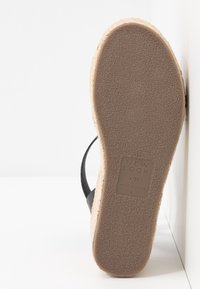 Sandale à bride noire avec une semelle en caoutchouc texturé de couleur brun clair. Comprend un intermédiaire en liège beige et des détails en étiquette embossée sur la semelle.
