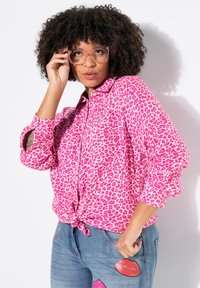 Rosa leopardmønster knap-up skjorte med en knyttet kant, parret med blå jeans med læbebeformede lapper og en tapered silhuet.