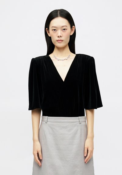 Haut en velours noir avec un décolleté en V et des manches ballon, associé à une jupe gris clair. Collier en argent simple avec des accents. Texture lisse.