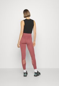 Svart ärmlös topp och höga maroon leggings med meshpaneler. Modellen bär svarta och turkosa sneakers med vita strumpor.