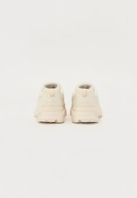 Scarpe sportive beige con tomaia in rete, dettagli testurizzati e suola ammortizzata, viste da dietro, con un design minimalista.