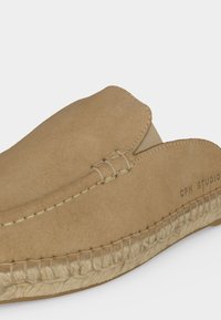 Espadrille en daim marron clair à enfiler avec coutures visibles et semelle en jute tressée, avec un petit logo « CPH STUDIOS » sur le côté.