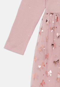 Dugih rukava ružičasta rebrasta majica spojena s ružičastom mrežastom suknjom s sjajnim zlatnim uzorcima u obliku ruža.