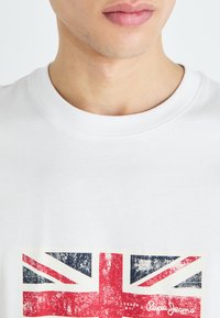 Camiseta de algodón blanca con un estampado retro de la Union Jack en rojo, azul y blanco, con un cuello redondo y mangas cortas.