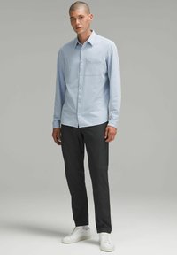 Cămașă butonată de culoare albastră deschisă, cu o buzunar pe piept, asortată cu pantaloni întunecați și adidași albi. Material neted, mâneci lungi și croială ajustată.