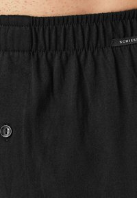 Shorts en coton noir avec une taille élastique, une fermeture à bouton unique et une texture douce. Étiquette de marque visible sur la taille.