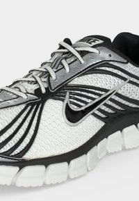 Άσπρο και μαύρο παπούτσι για τρέξιμο Nike με υφή από δίχτυ, μαύρο λογότυπο Swoosh, λευκά κορδόνια και διαχωρισμένη σόλα για ευελιξία.