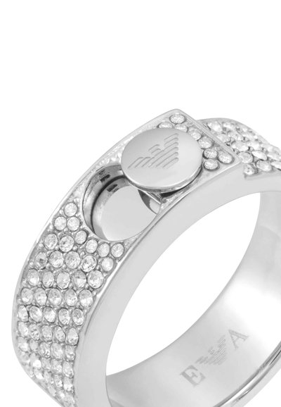 Silverring med en strukturerad band med cirkulära klara ädelstenar, en cirkulär knapp inlagd med en logotyp och en polerad inre yta.