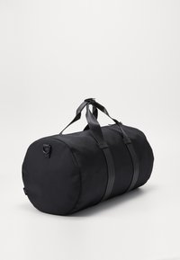 Bolsa deportiva cilíndrica negra, fabricada en tejido texturizado, con asas y bandas resistentes; diseño elegante y funcional con un detalle mínimo.