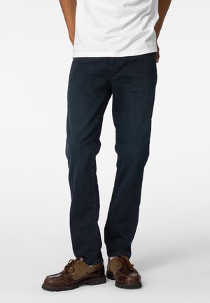 Mørkeblå denimjeans med rette ben, utstyrt med fem lommer og subtile sømdetaljer. Brukt med brune sko og en hvit t-skjorte.