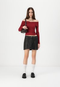 Crvena off-the-shoulder bluzica dugih rukava, crna mini suknja od kože s vidljivim šavovima, u paru s crnim loafers cipelama i bijelim čarapama do koljena.