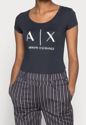 Mørkeblå t-shirt med korte ærmer og scoop-halsudskæring, prydet med et hvidt "A|X Armani Exchange" logo. Sammenstylet med stribede højtaljede bukser.