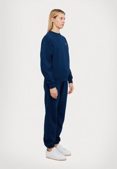 Marineblauw sweatshirt en sweatpants set van een zacht materiaal met ribgebreide boorden, gecombineerd met witte sneakers met een lichtbruine zool.