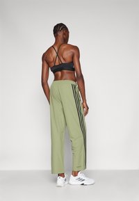 Sportovní outfit s černou sportovní podprsenkou a světle zelenými kalhotami s černými bočními pruhy. Model má na sobě bílé tenisky a ukazuje zkrácenou siluetu.