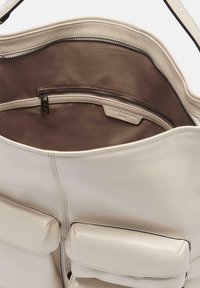 Kremowa skórzana torba na ramię z brązowym materiałowym wnętrzem, pojedyncza kieszeń główna na zamek błyskawiczny oraz dwie kieszenie przednie z klapką.