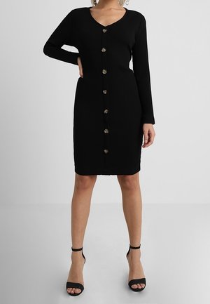 Robe noire côtelée à manches longues, col en V, avec des boutons sur le devant. Caractérisée par une coupe ajustée et une texture lisse.