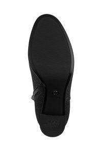 Suola nera della scarpa con uno schema di grip testurizzato, caratterizzata da una forma arrotondata e un profilo piatto. Dettaglio della cerniera laterale visibile nella parte superiore.