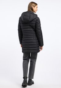 Zwarte pufferjack met een capuchon, voorzien van horizontale quilted strepen, een langere snit en een zachte, glanzende textuur. Draagt met grijze broek en zwarte laarzen.