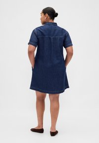 Jeansklänning i mörkblått, korta ärmar, med krage, fickor på sidorna och rak nederkant. Mjuk textur med subtila sömndetaljer.