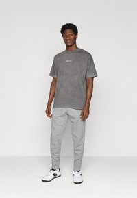 Γκρι βαμβακερό μπλουζάκι με στρογγυλή λαιμόκοψη, συνδυασμένο με ανοιχτό γκρι φόρμες. Λευκά αθλητικά παπούτσια με μαύρες λεπτομέρειες ολοκληρώνουν το σύνολο. Χωρίς σχέδια ή γραφικά.