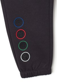 Donkergrijze trainingsbroek met een geribbelde enkelmanchet, voorzien van vijf ronde grafische patches in blauw, rood, groen, zwart en wit langs de zijkant.