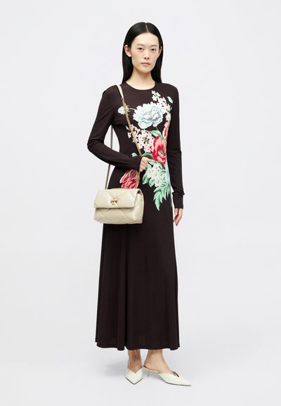 Czarna sukienka z długim rękawem o wyrazistym floralnym wzorze, w połączeniu z kremową, pikowaną torebką i białymi szpilkami, prezentowana na neutralnym tle.