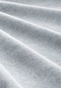 Tessuto in denim blu chiaro, caratterizzato da una texture liscia con un sottile motivo a spina di pesce diagonale e una caduta morbida, mostrato in strati piegati.