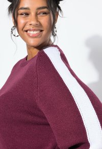 Maglione a maglia bordeaux con scollo rotondo e dettagli a strisce verticali bianche sulla spalla, caratterizzato da una finitura texturizzata.