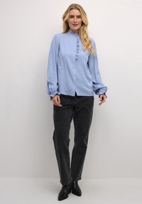 Light blue blouse with a high ruffled collar, button front, and long balloon sleeves, paired with black high-waisted jeans and ankle boots.
