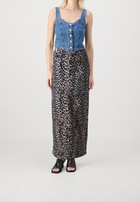 Top corto de mezclilla con detalles de botones combinado con una falda larga de estampado de leopardo. Zapatos negros de punta abierta completan el look.