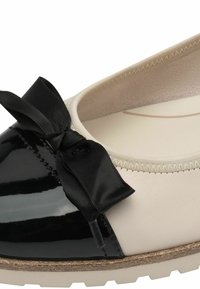 Punta in vernice nera con un fiocco, tomaia in pelle crema, interno texturizzato e suola marrone chiaro con un leggero motivo di battistrada.
