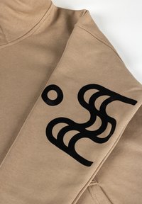 Beežist kangast varrukas musta abstraktse geomeetrilise mustriga, millel on ringid ja kõverad jooned, volditud rõivaesemel.