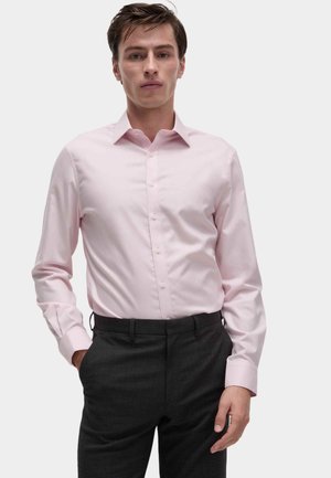 Chemise boutonnée rose clair avec un col classique et des manches longues, associée à un pantalon gris foncé, présentée de face.