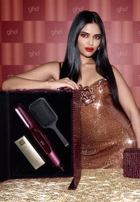 Haarstyling-Set in einem strukturierten, burgunderfarbenen Etui. Enthält eine schwarze Paddle-Bürste, einen glänzenden, eleganten pinken Glätter und eine goldene Produktbox.