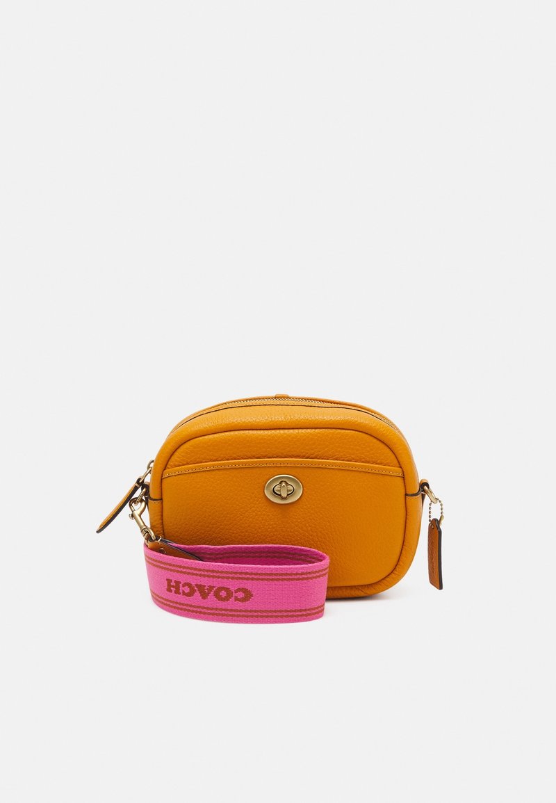 Žlutá kožená kabelka přes rameno zaobleného tvaru, s uzávěrem ve zlatém odstínu a růžovým textilním popruhem s logem "COACH".