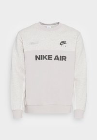Ljusgrå Nike Air sweatshirt med långa ärmar och ribbade muddar, med svart "NIKE AIR"-text och logotyper på bröstet.