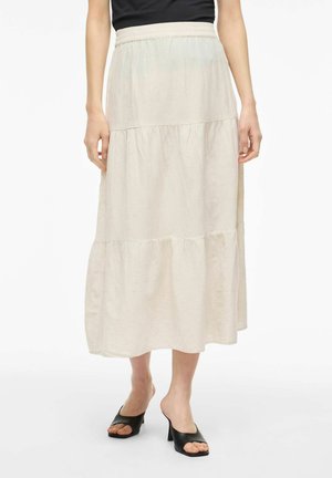 Femme portant une jupe midi beige à volants avec une taille élastique, associée à des mules à talons ouvertes noires et un haut noir.