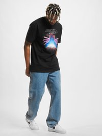 Svart t-skjorte med et grafisk motiv av hender og en basketball, kombinert med løse blå jeans og hvite sneakers med svarte detaljer.