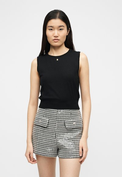 Femme aux cheveux noirs et lisses portant un haut noir sans manches et un short taille haute à carreaux noir et blanc avec des poches avant.