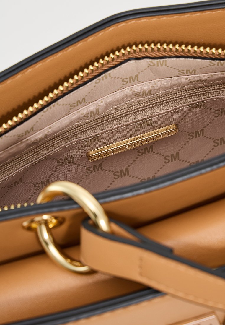 Wnętrze torebki skórzanej w kolorze tan z beżowym wykończeniem w wzór "SM", kieszonką na zamek błyskawiczny oraz złotą tabliczką z nazwą marki.