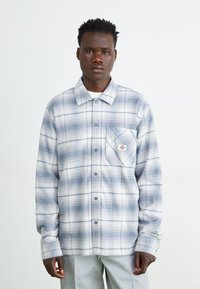 Camicia a quadri con bottoni nei toni azzurro chiaro e grigio, tessuto morbido con taschino sul petto, dotata di una patch con logo e un design di colletto classico.